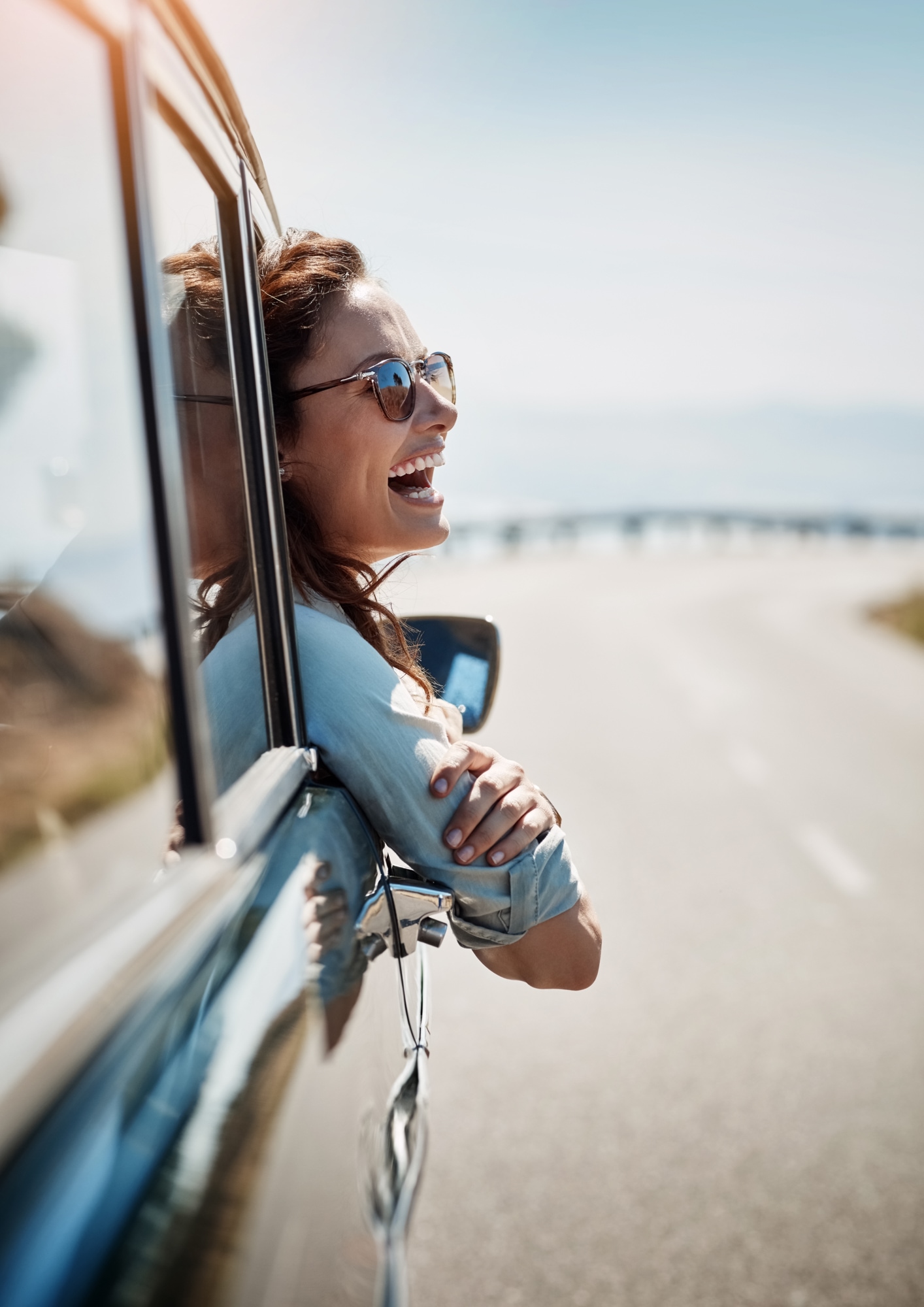 A woman hanging out of the car window smiling and laughing